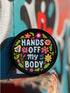 Glossy black pinback button with floral art and bold white text that reads “Hands Off My Body.” Feminist political button featuring bright pastel flowers in pink, red, orange, and yellow. Metal pin with durable safety pin back, shown in various settings: held by hand, displayed on pedestal, and against colorful street art. Available in 2" and 3" sizes, perfect for backpacks, jackets, tote bags, or as a gift for feminist allies and book lovers.